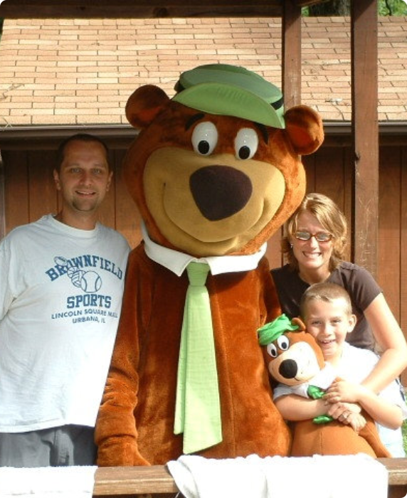 A family smiles while posing with a friendly bear mascot