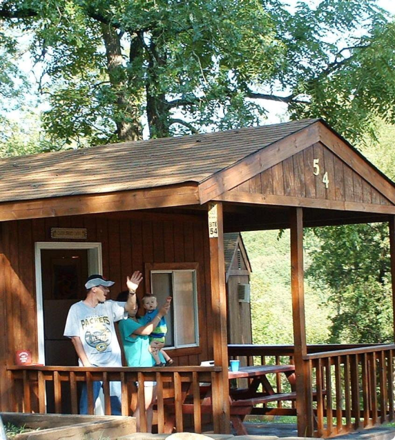 A couple stands on the porch of a rustic cabin