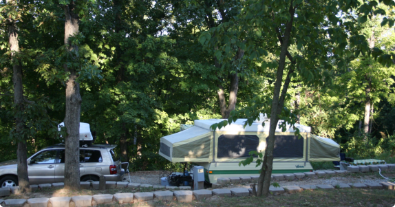 A tent set up beside a parked car in a serene wooded area