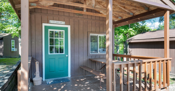 A rustic cabin featuring a green door and a welcoming porch