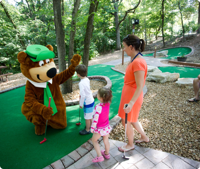 A woman and two children stand together, gazing at a bear in a natural setting.