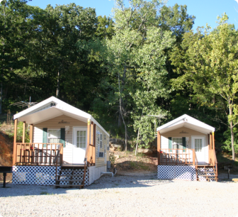 Two small cabins featuring porches and decks, set in a natural outdoor environment.