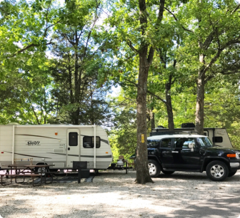 A camper and an RV parked side by side in a green park