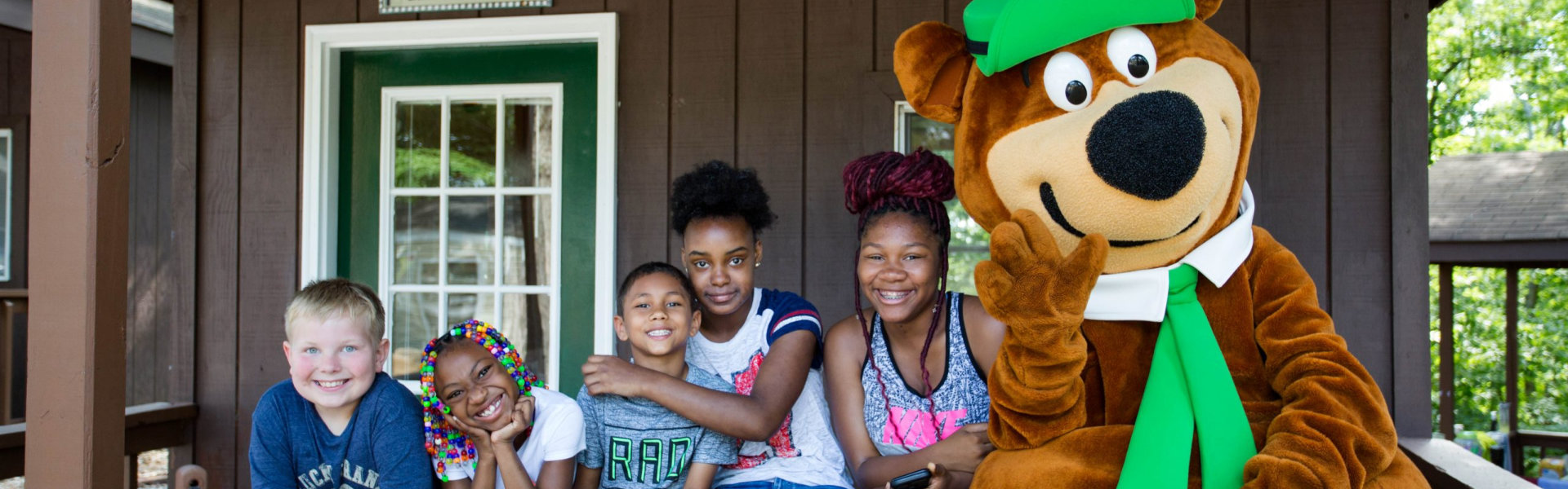 A group of smiling children poses with bear mascot