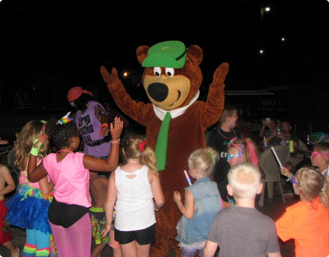 A group of children joyfully gathered around a colorful mascot